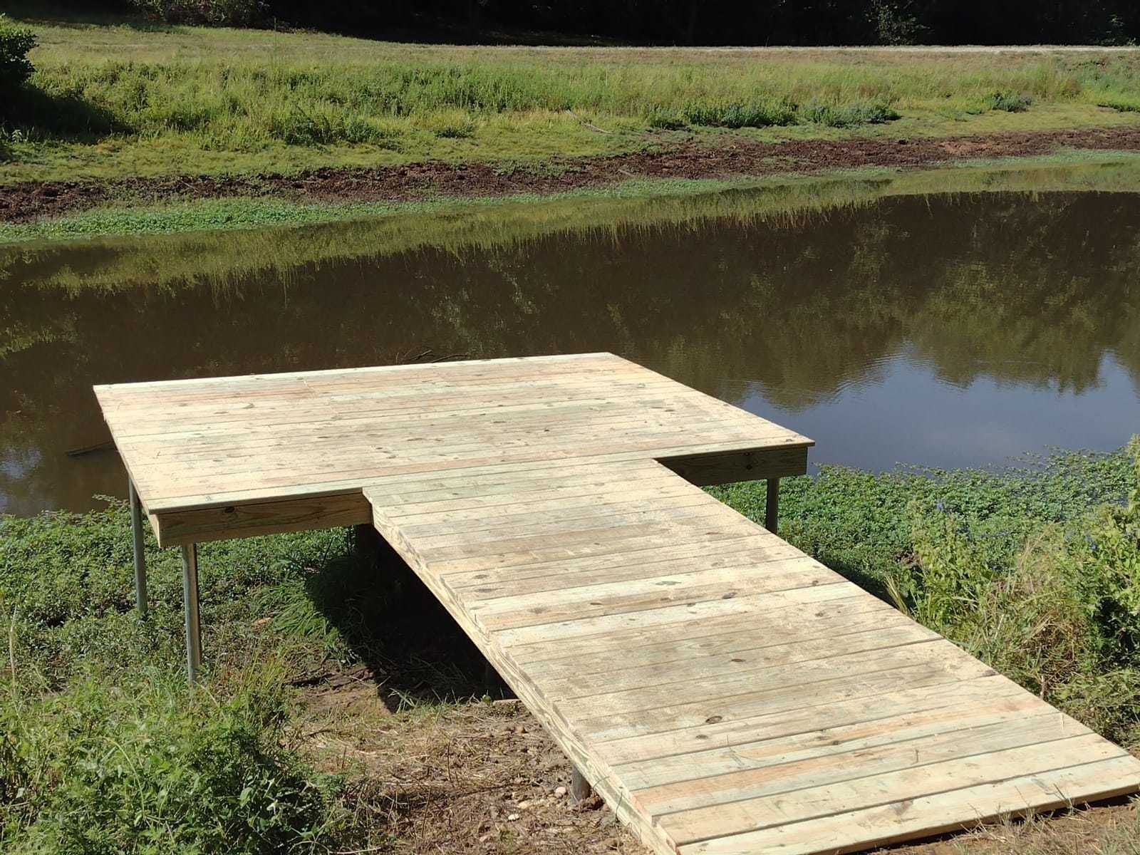Wooden dock extending over a calm pond in a grassy outdoor area