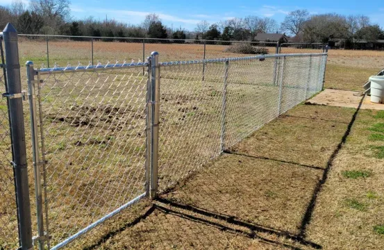 Chain-link fence enclosing a grassy yard under a blue sky