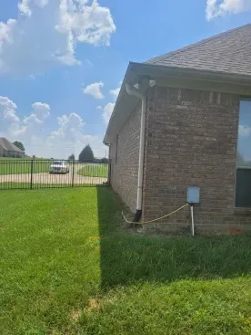 Brick house side yard with green lawn, fenced backyard, utility box, and blue sky with clouds