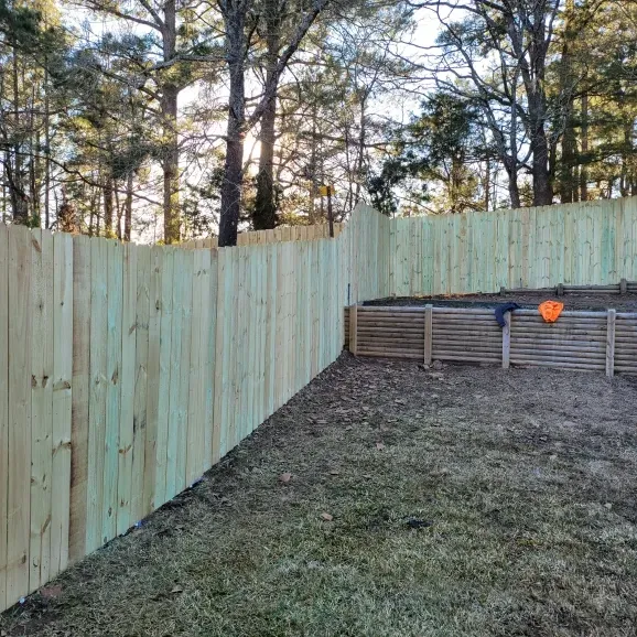 Backyard with a tall wooden fence, raised garden bed, and trees beyond the yard