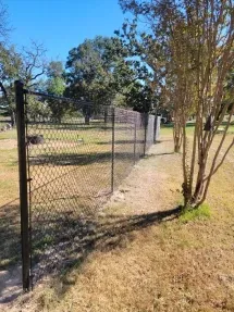 Chain-link fence along a grassy path with trees under a clear blue sky.