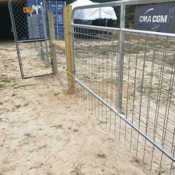 Wire fence gate beside a sandy path with a tent and chain-link fence in the background