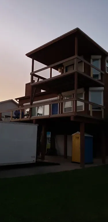 Three-story wooden house at dusk with lit windows and a white truck in front