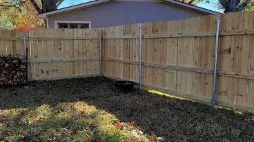 Backyard corner with a wooden privacy fence, fallen leaves, and a house in the background