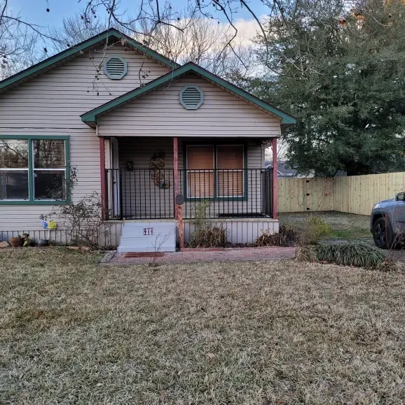 Small beige house with green trim, front porch, and a yard at dusk.