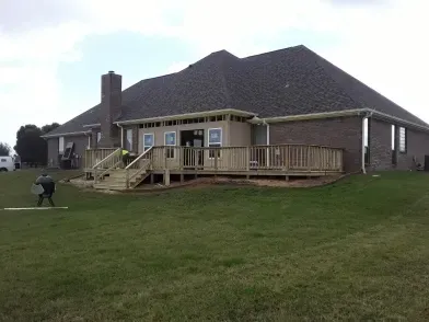 Brick house with raised wooden deck and stairs on a grassy lawn under a cloudy sky