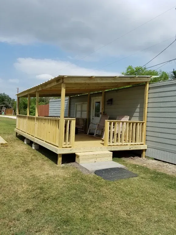 Small wooden front porch with ramp attached to a beige mobile home on a grassy lawn