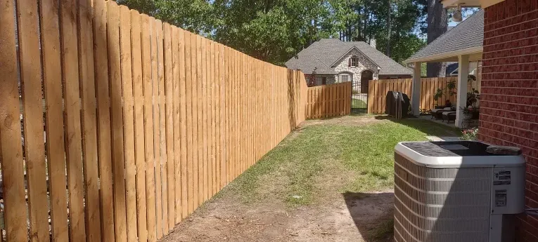 Wooden privacy fence along a grassy backyard path beside a house and air conditioner unit