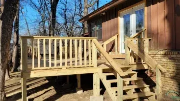 Wooden deck with stairs attached to a brown house in a wooded yard