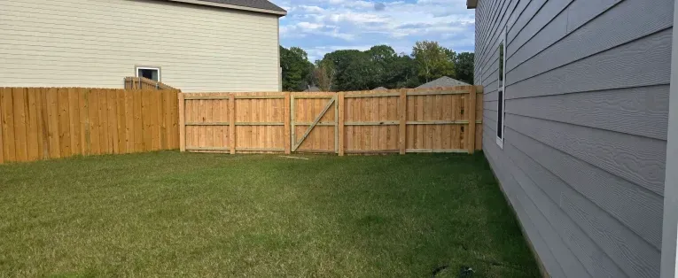 Backyard lawn bordered by wooden fence and gray house siding