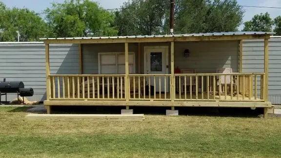 Small white mobile home with a covered wooden porch in a grassy yard.