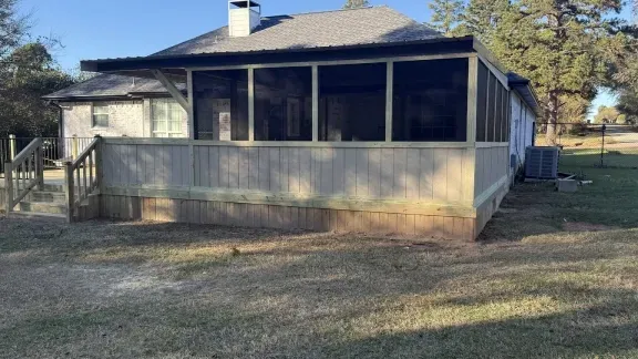 Weathered house with a screened front porch and low ramp in a grassy yard.