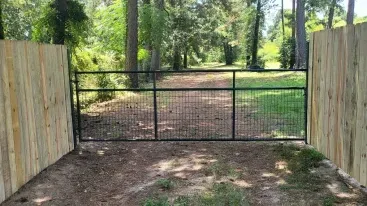 Closed black metal gate between wooden fences at the entrance to a wooded dirt path