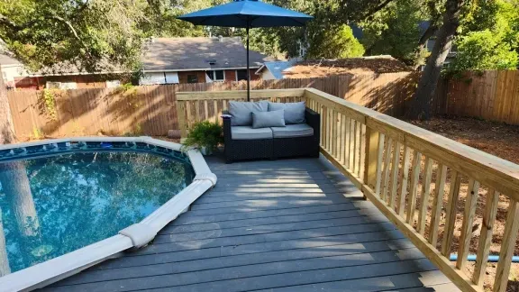 Backyard deck beside a blue pool, with a gray loveseat and blue umbrella