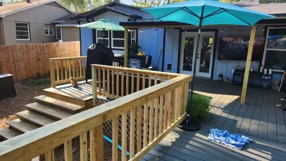 Backyard deck with steps, wooden railing, and blue patio umbrella beside a house