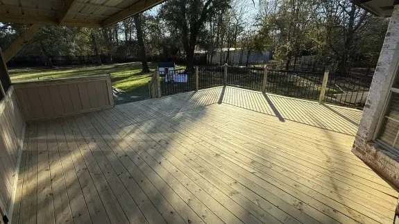 Wooden deck under a covered patio overlooking a fenced yard with trees and a picnic table.
