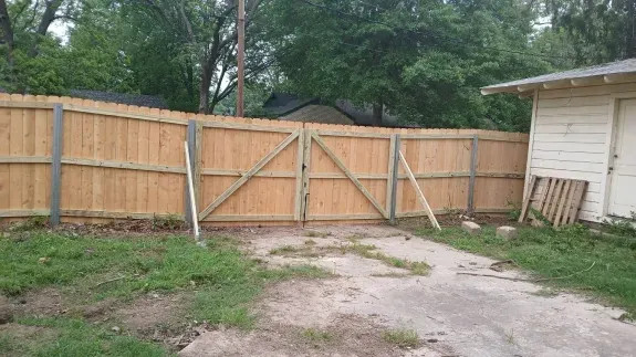 Wooden backyard fence with double gate beside a house and grassy yard with a dirt path