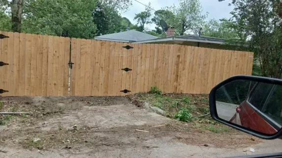 Wooden fence across a muddy driveway, viewed from inside a car on a rainy day.