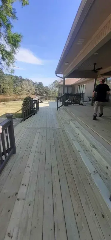 Wooden deck beside a house overlooking a grassy yard, with a person walking near the porch.