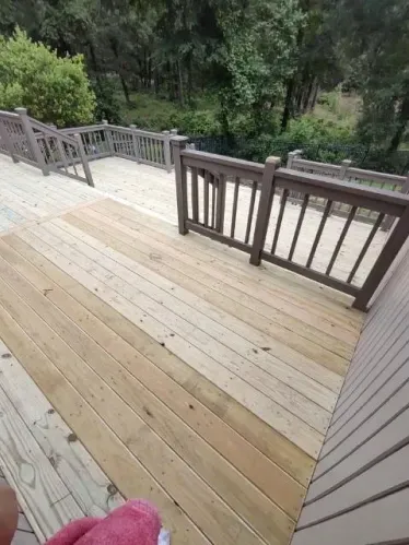 Wooden deck with railings overlooking a green wooded area and steps leading down to a lower level.