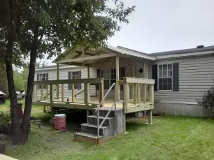 Small raised porch with steps attached to a gray house in a grassy yard.