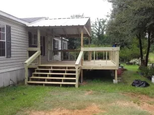 Back porch with wooden steps and railing attached to a gray house in a grassy yard