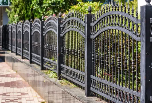 Ornate black metal fence along a sidewalk beside greenery and a paved path