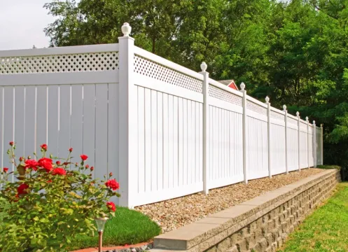 White vinyl fence along a garden bed with red flowers and green trees behind it
