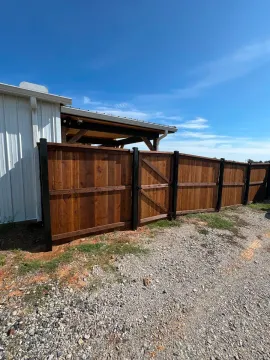 Wooden fence and open gate beside a white metal shed on a gravel lot under a blue sky