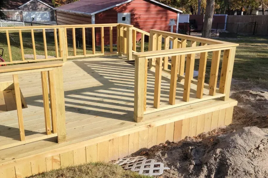 Wooden deck under construction with railings, steps, and a house in the background