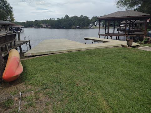 Lakeside dock with grassy shore, wooden platform, and a red kayak by calm water under cloudy sky