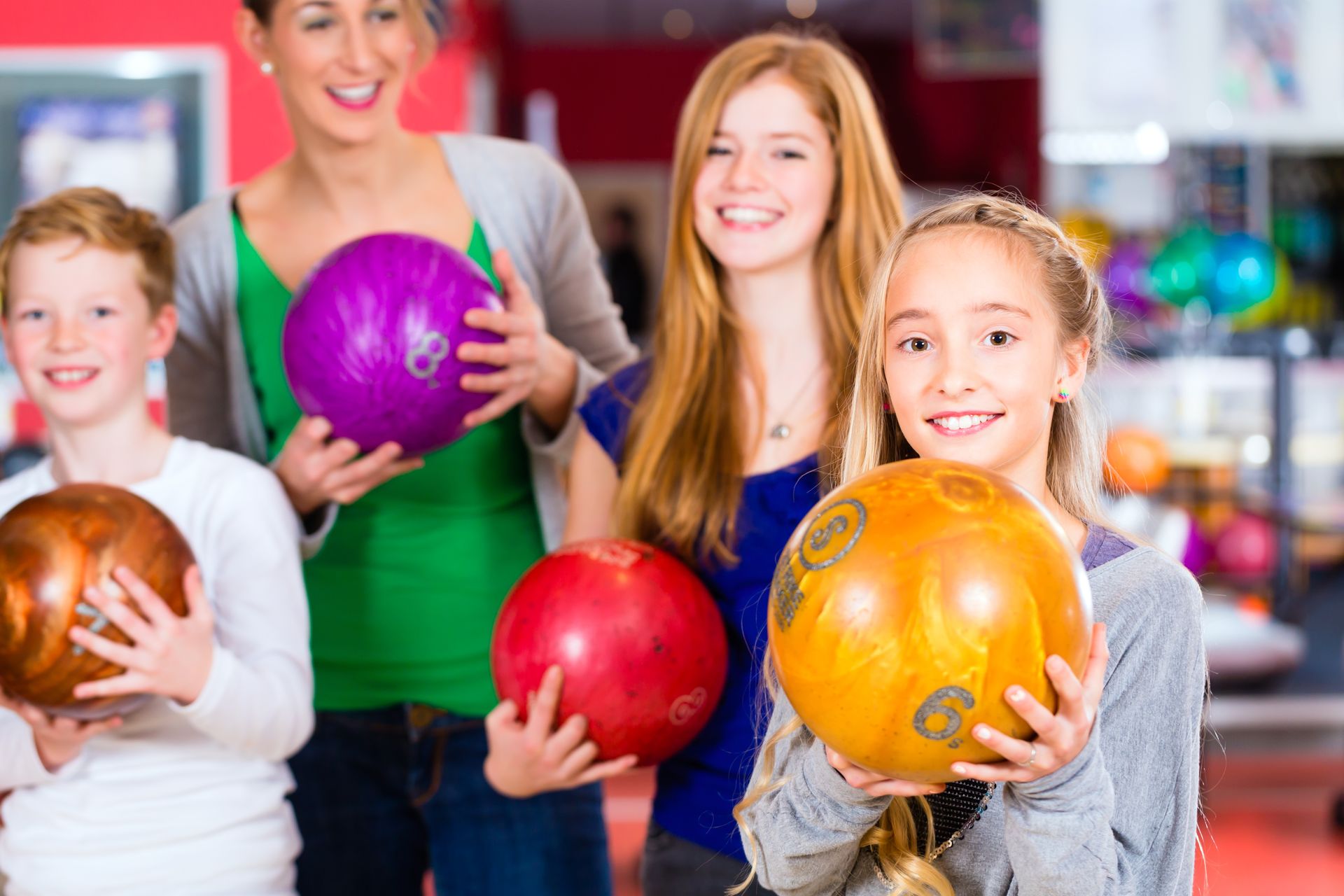 Group of smiling kids holding bowling balls at a bowling alley