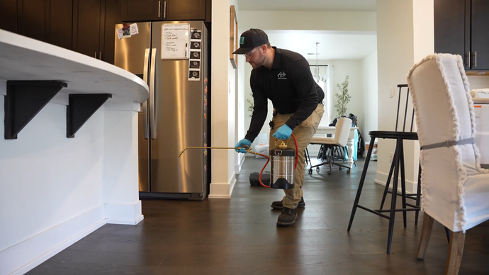 Person cleaning a kitchen floor near a stainless fridge and dining chairs