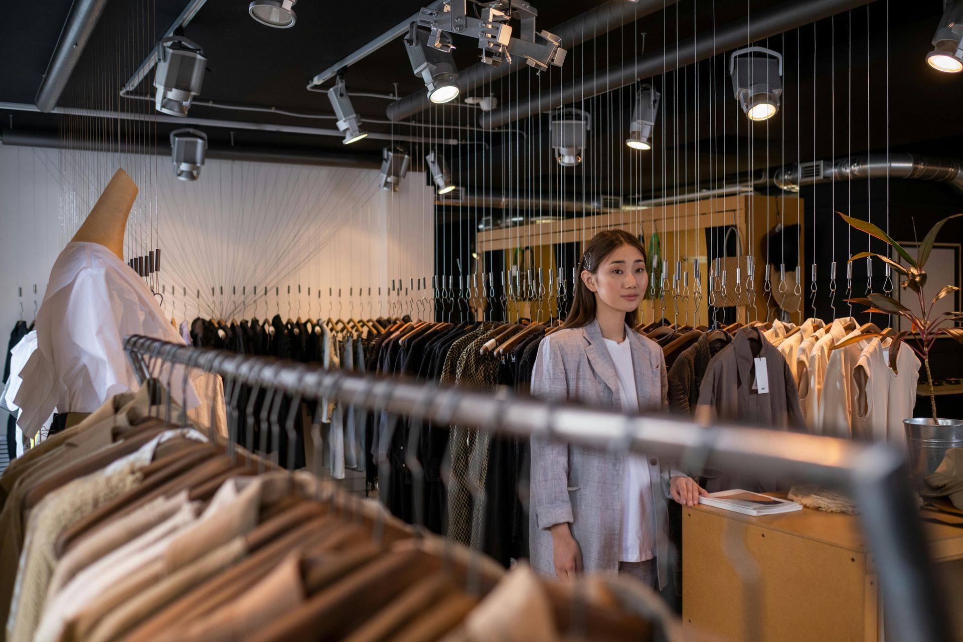Clothing boutique interior with hanging garments and a woman standing among racks under warm lights