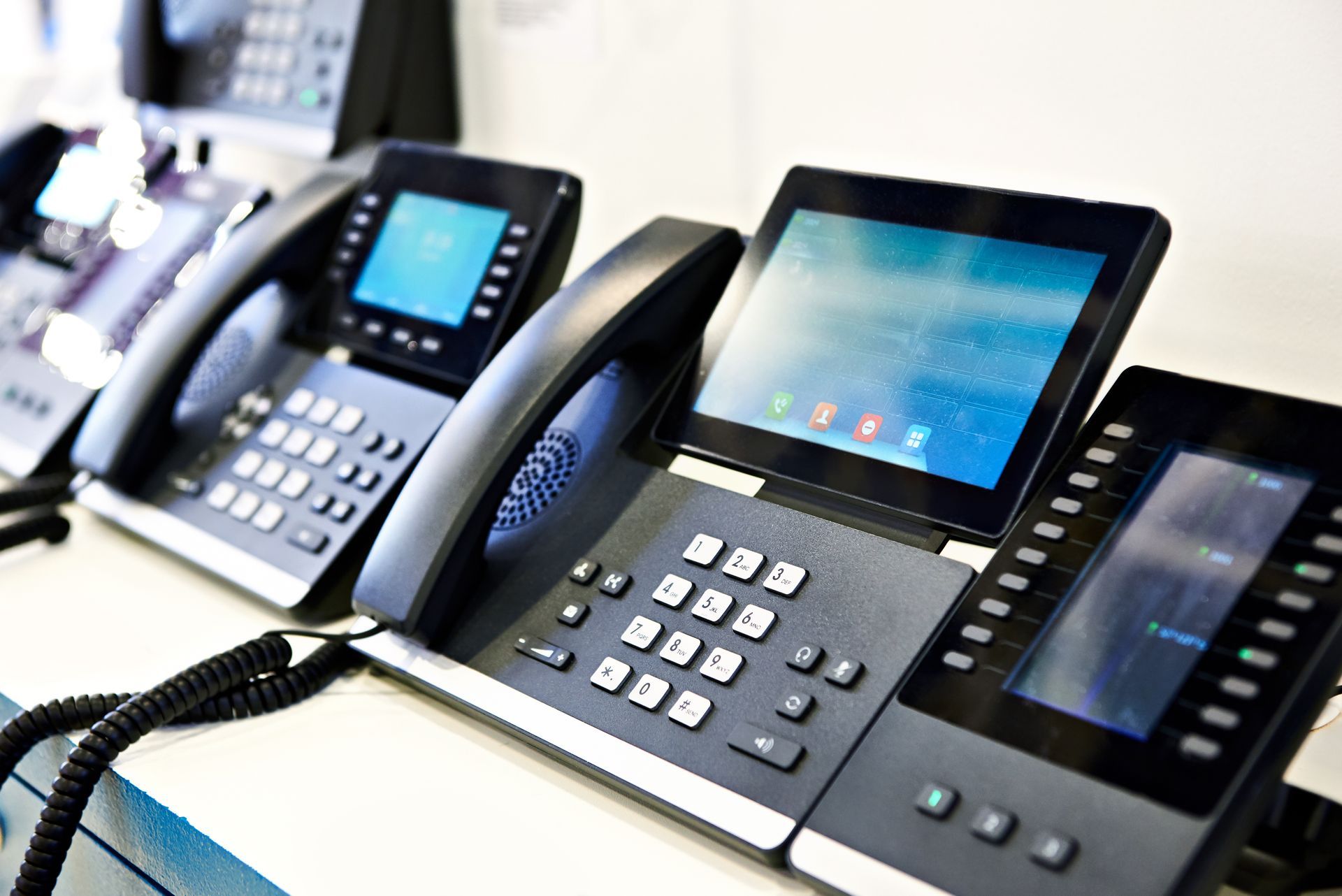 Row of office desk phones with touchscreen displays and keypad buttons on a table
