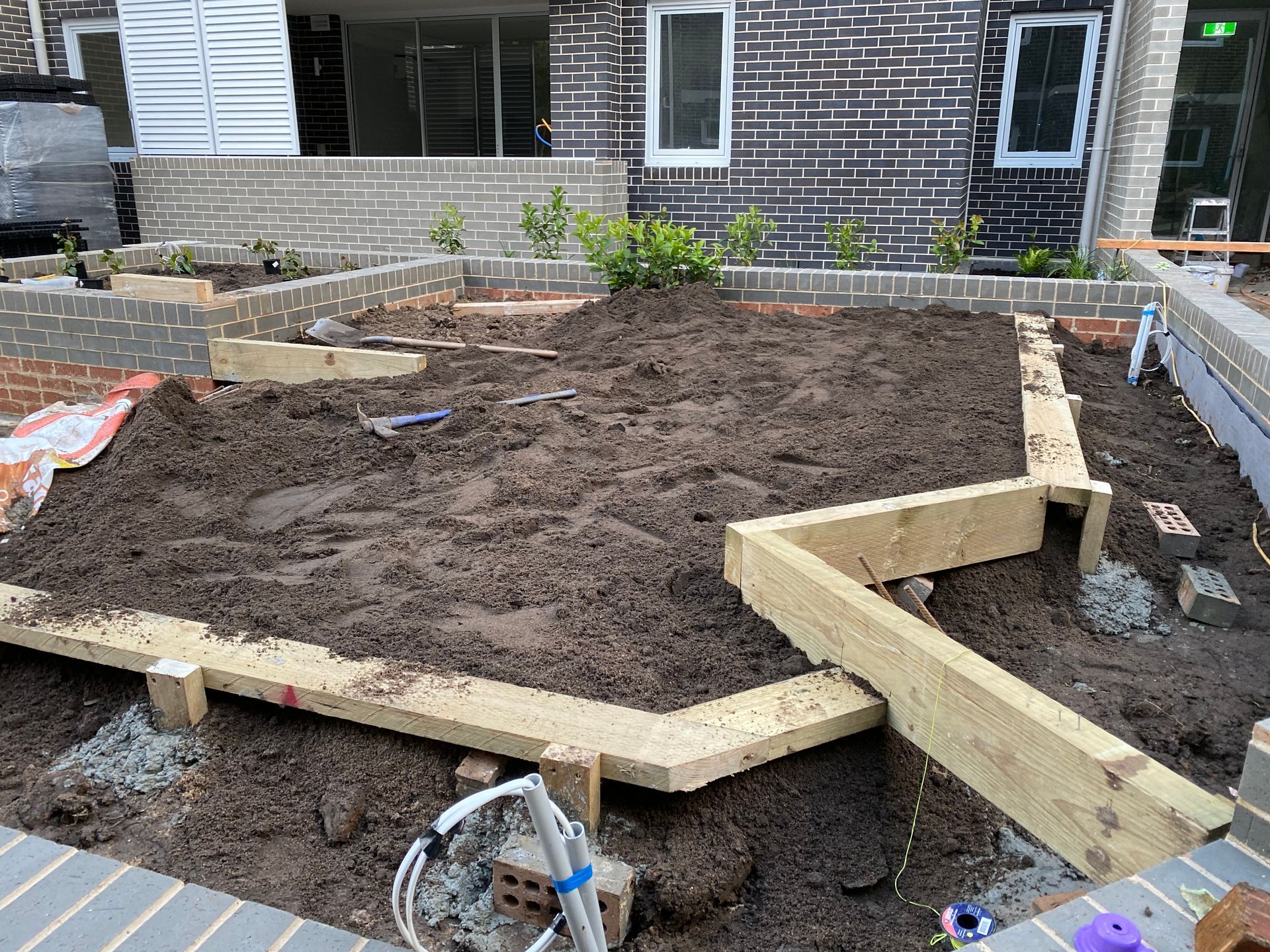 Garden bed under construction with wooden frame, soil, and brick retaining walls.