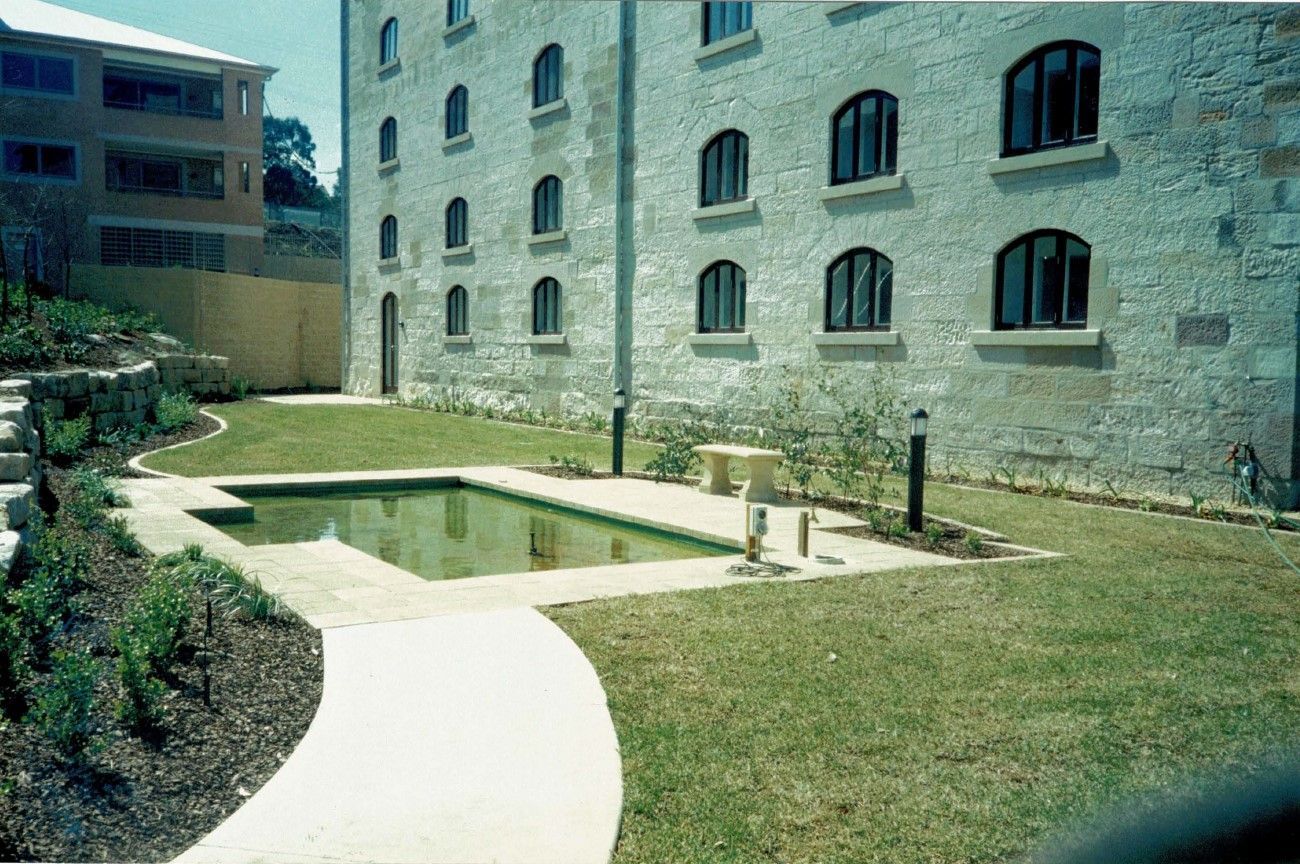 Stone building courtyard with a small rectangular pond, lawn, and curved white path
