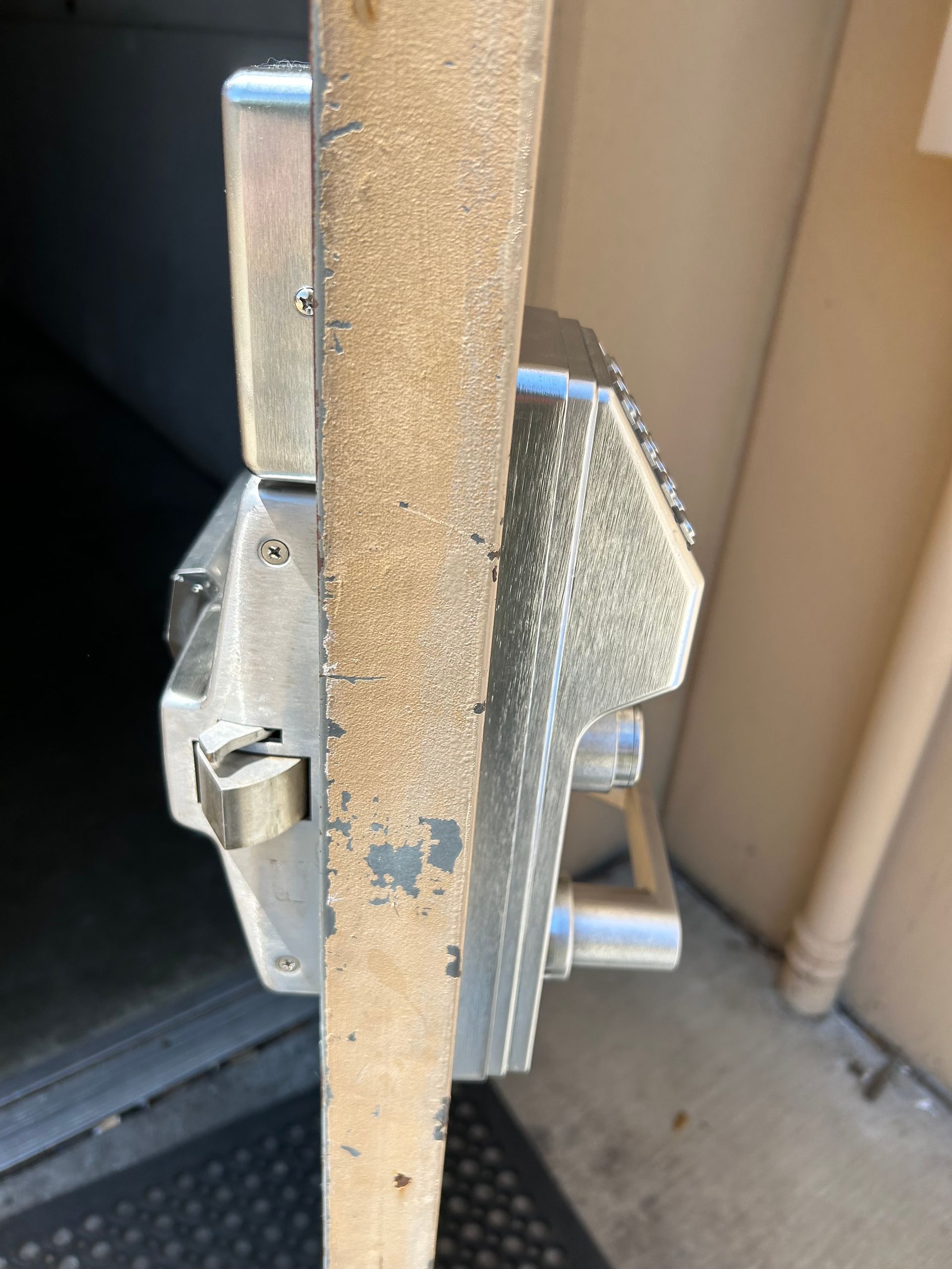 Close-up of a door lock with a handle. The lock is silver, doorframe is beige.