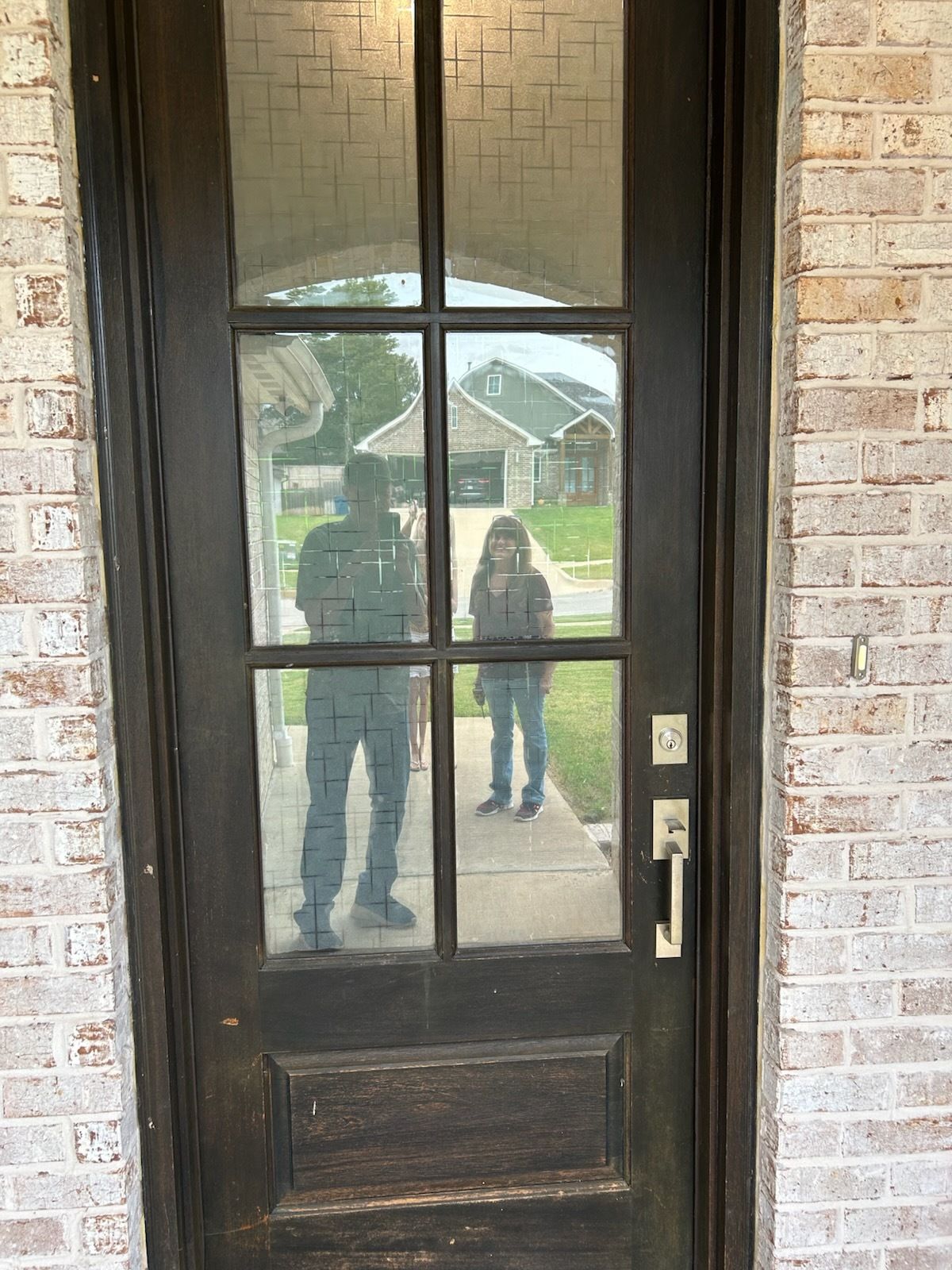 Dark wooden front door with glass panes reflecting two people standing outside.