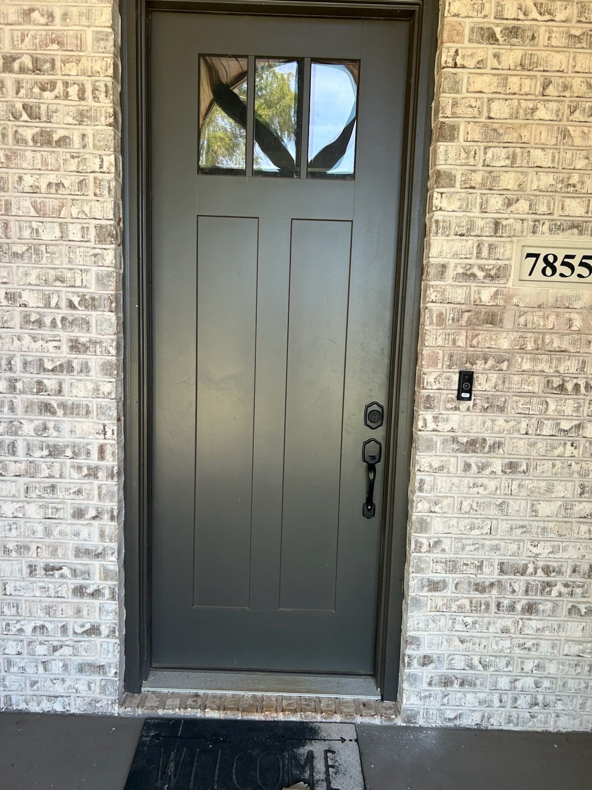 Dark gray front door in a brick entryway with the house number 7855 on the right.