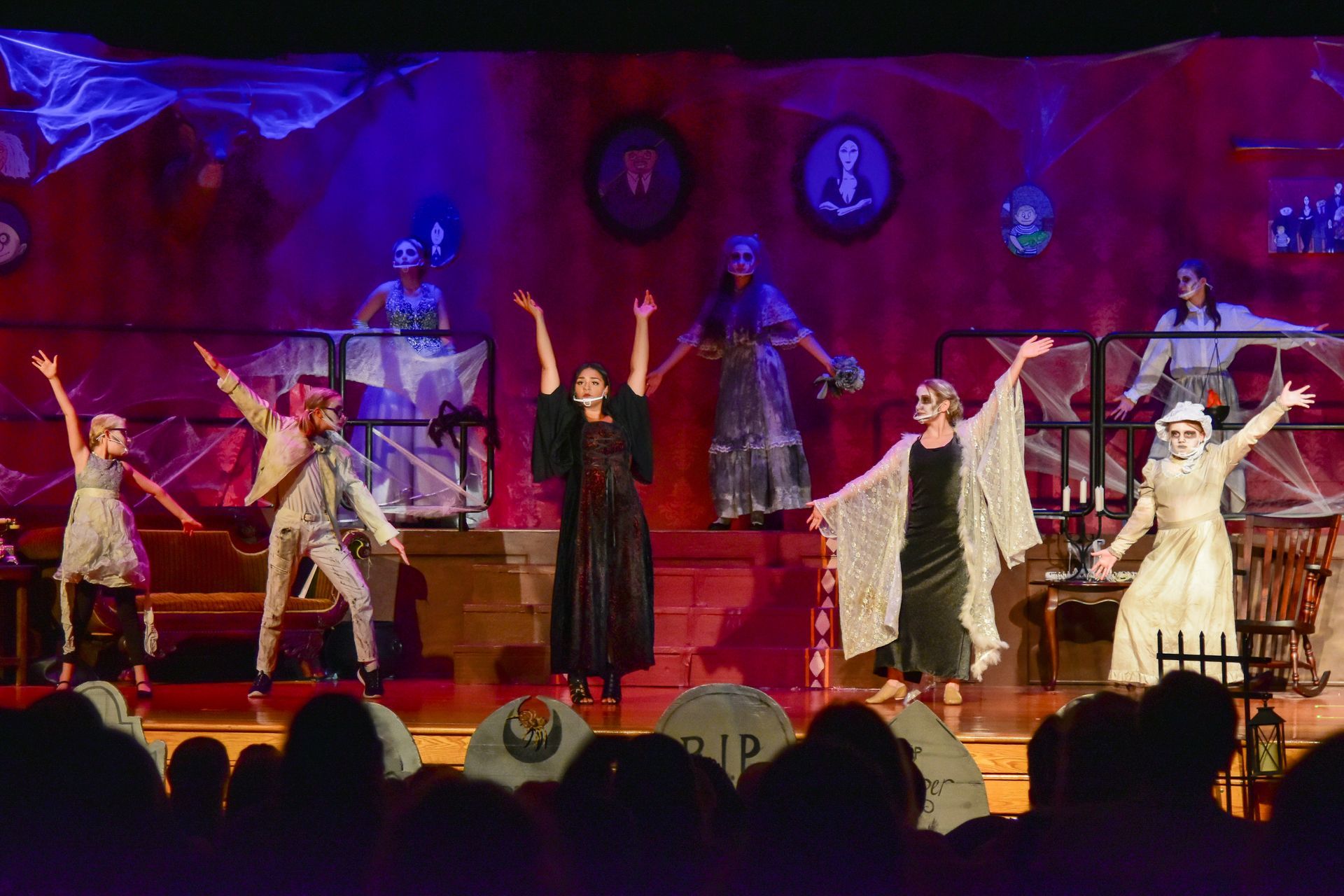 A stage with performers in ghostly costumes, arms raised, with a dark backdrop, a set for a play.