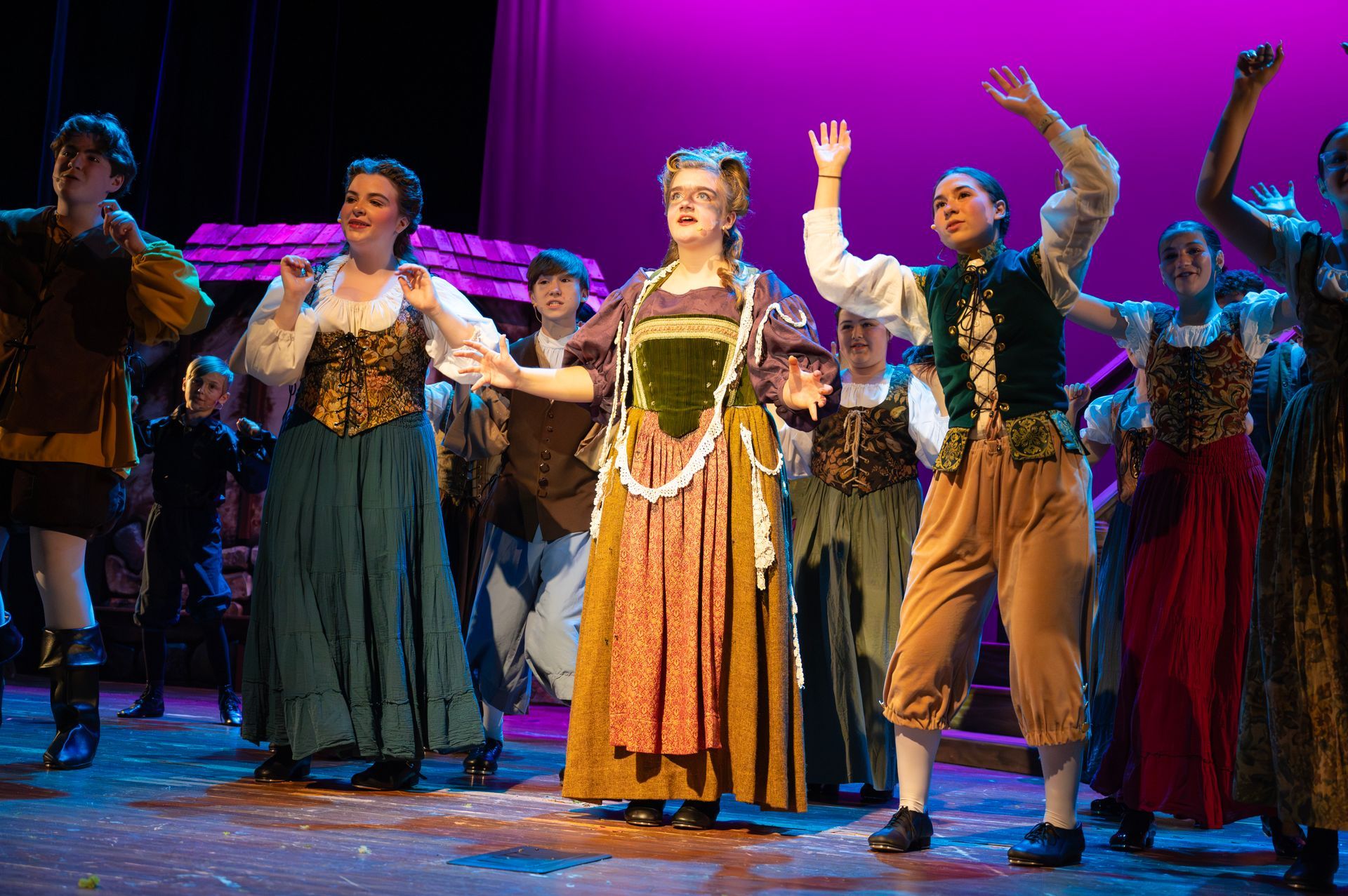 A stage production featuring a group of actors in colorful, period costumes performing with expressive gestures.