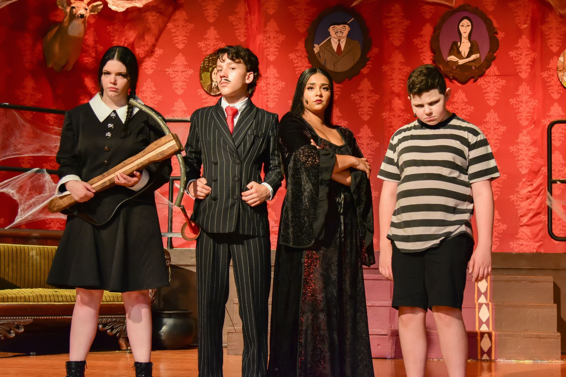 Four actors dressed as Addams Family characters on a stage: Wednesday, Gomez, Morticia, and Pugsley.