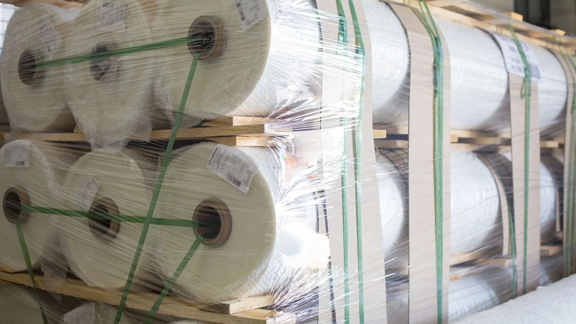 A bunch of rolls of plastic wrap are stacked on top of each other on wooden pallets.
