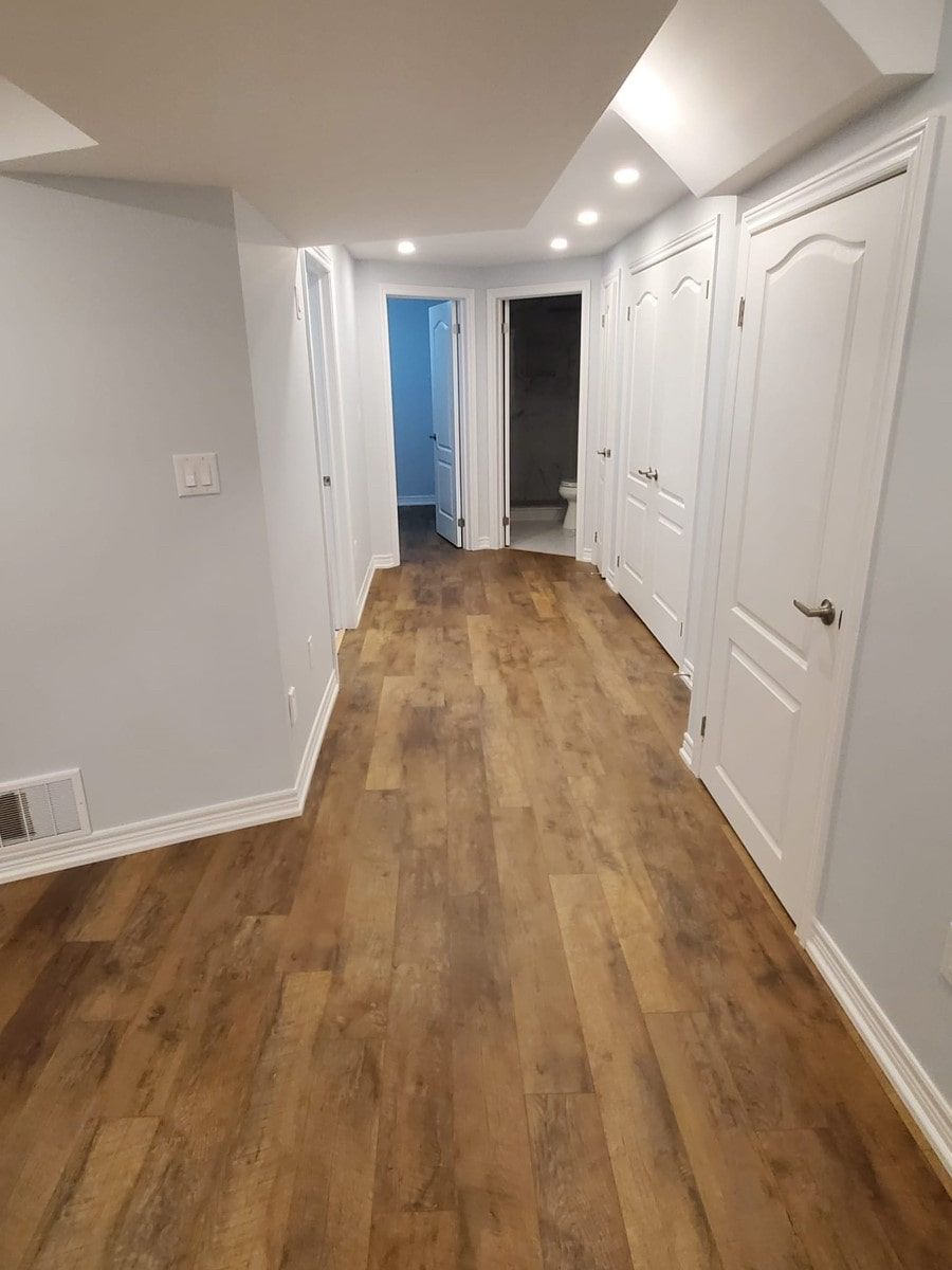 Hallway with wood-look flooring, light gray walls, white doors, and recessed ceiling lights.