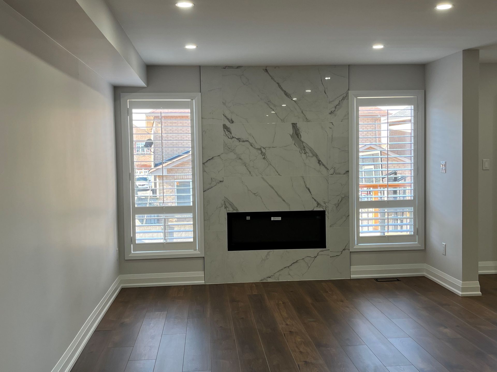 Living room with white marble fireplace, two windows, and dark wood floors.
