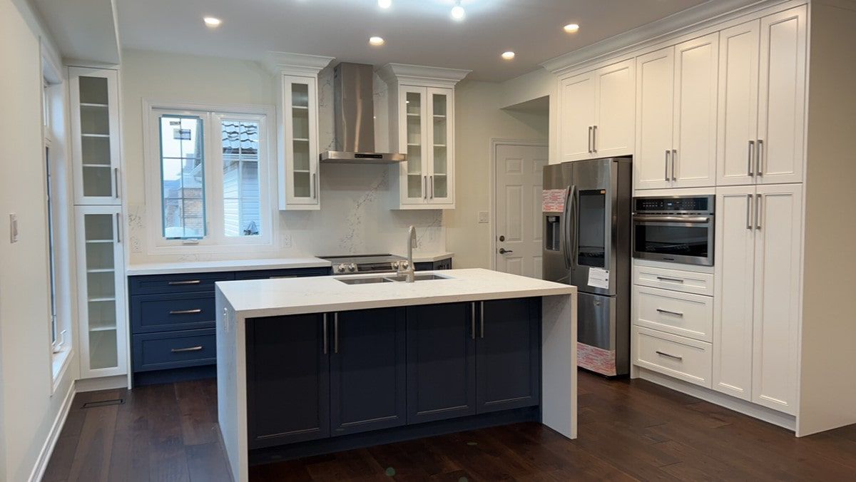 Modern kitchen with navy and white cabinets, stainless steel appliances, and an island.