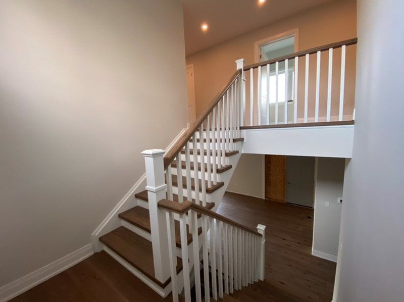 Staircase with wooden steps and white railing. Leads to a landing and upper level. Beige walls, dark flooring.