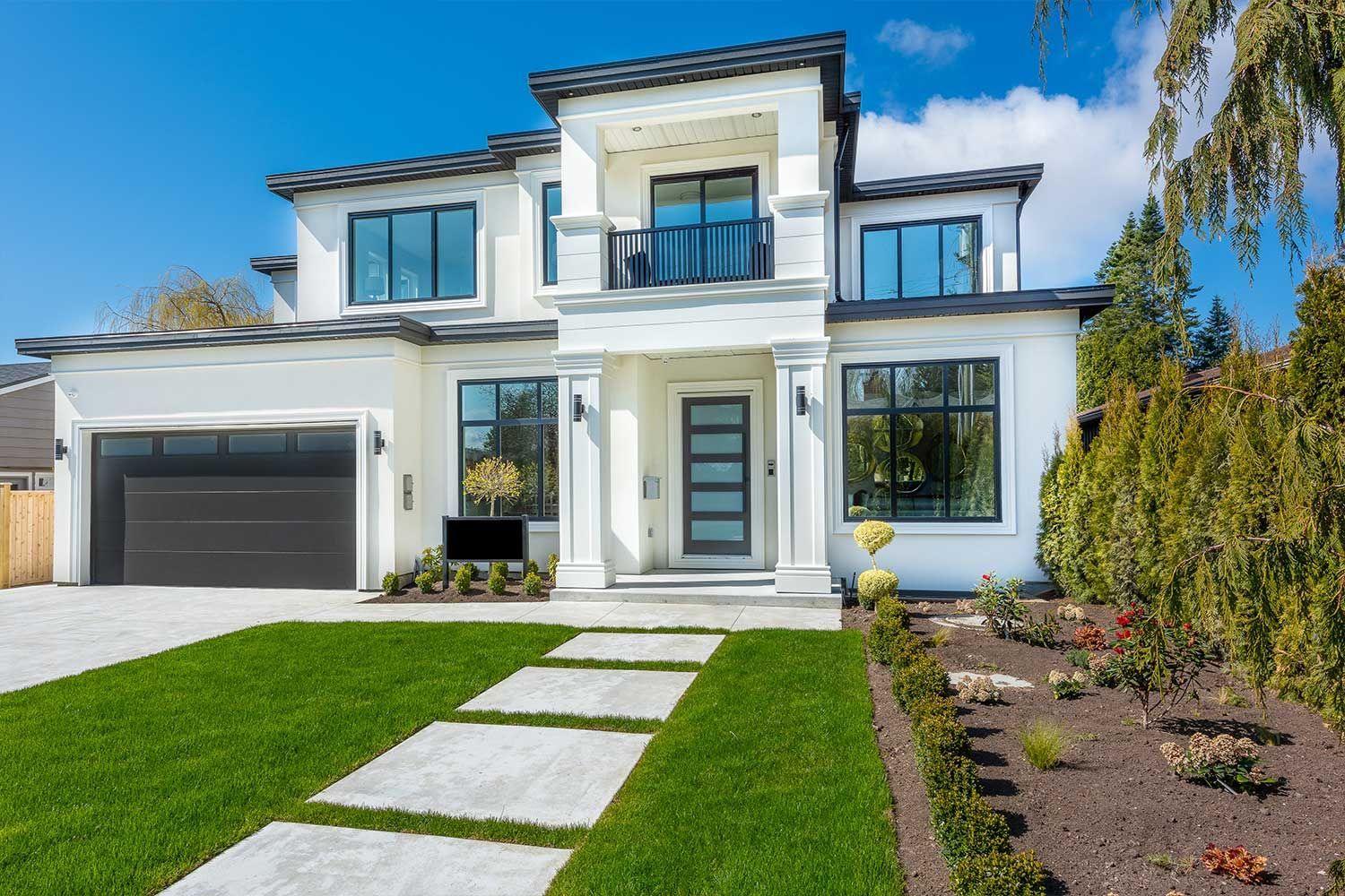 A large white house with a black garage door is sitting on top of a lush green lawn.