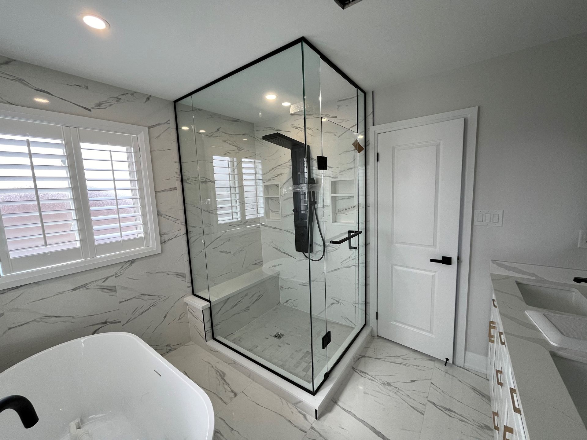Modern bathroom with glass shower enclosure, white marble tile, and white door.